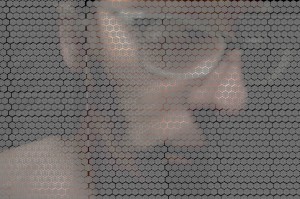 MATTHEW SWARTS A CLOSE-UP OF A PERSON’S FACE WITH GLASSES, PARTIALLY OBSCURED BY A GRID OF CIRCULAR, HONEYCOMB-LIKE PATTERNS OVERLAYING THE IMAGE. THE CONTEMPORARY VISUAL EFFECT CREATES A TEXTURED, ABSTRACT LOOK OVER THE PORTRAIT.
