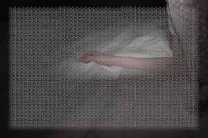 MATTHEW SWARTS A PERSON’S PALE HAND AND ARM REST ON WHITE FABRIC, PARTIALLY COVERED BY A SHEER, PATTERNED CLOTH IN A DIMLY LIT SETTING. THIS CONTEMPORARY SCENE FEELS CALM AND DELICATE, LIKE A STILL FROM AN INTIMATE DOCUMENTARY WITH SOFT SHADOWS.