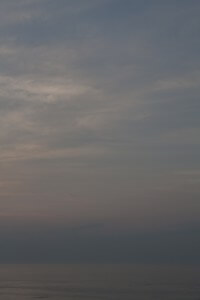 MATTHEW SWARTS A CALM OCEAN UNDER A MOSTLY CLOUDY SKY AT DUSK, WITH SOFT PASTEL SHADES OF BLUE, PINK, AND PURPLE BLENDING ON THE HORIZON AND REFLECTING GENTLY ON THE WATER.