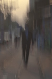MATTHEW SWARTS A PERSON IN A SUIT WALKS DOWN A CITY SIDEWALK AT DUSK IN OSLO. THE IMAGE IS HEAVILY BLURRED, CREATING A DISTORTED, DREAMLIKE SCENE WITH INDISTINCT SHAPES AND MUTED COLORS.