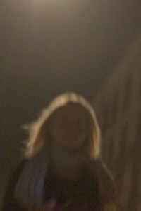 MATTHEW SWARTS A BLURRY, OUT-OF-FOCUS IMAGE OF A PERSON WITH LONG HAIR STANDING OUTDOORS AT NIGHT IN COPENHAGEN, ILLUMINATED BY A SOFT LIGHT ABOVE. THE DARK BACKGROUND ADDS TO THE ATMOSPHERIC CITY SCENE.