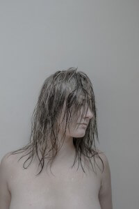 MATTHEW SWARTS A PERSON WITH WET, TANGLED HAIR COVERING THEIR FACE LOOKS OFF TO THE SIDE AGAINST A PLAIN BACKGROUND.