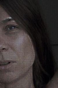 MATTHEW SWARTS CLOSE-UP OF A PERSONS FACE, PARTIALLY OBSCURED BY DARK HAIR, RENDERED IN A PIXELATED STYLE WITH VISIBLE RED, GREEN, AND BLUE SUBPIXELS.