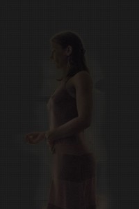 MATTHEW SWARTS A WOMAN IN A DARK PINK DRESS STANDS IN PROFILE AGAINST A DARK BACKGROUND.
