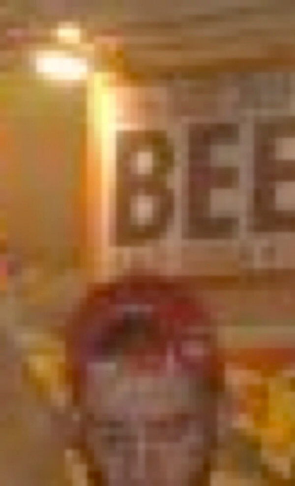 MATTHEW SWARTS A blurry image showing the top of a persons head in the foreground and a large sign in the background with the word BEER partially visible. The lighting is warm and the scene appears to be indoors.