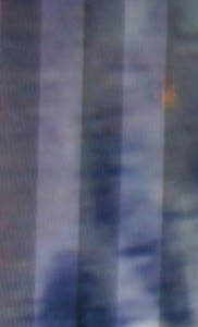 MATTHEW SWARTS A BLURRY, ABSTRACT IMAGE WITH VERTICAL GRAY AND BLUE STREAKS AND A SMALL ORANGE SPOT NEAR THE UPPER RIGHT CORNER. THE OVERALL APPEARANCE IS DISTORTED, AS IF VIEWED THROUGH A SCREEN OR FILTER.