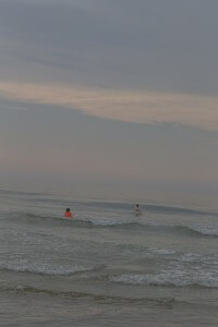 MATTHEW SWARTS TWO CHILDREN PLAY IN THE GENTLE WAVES OF THE OCEAN UNDER A SOFT, CLOUDY SKY. ONE CHILD WEARS AN ORANGE LIFE VEST.