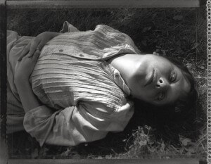 MATTHEW SWARTS A PERSON IN A STRIPED BUTTON-UP SHIRT LIES ON GRASS, GAZING UP AT THE CAMERA WITH ONE HAND ON THEIR STOMACH. THIS BLACK AND WHITE IMAGE BLENDS VINTAGE STYLE WITH CONTEMPORARY PHOTOGRAPHY FOR A STRIKING VISUAL EFFECT.