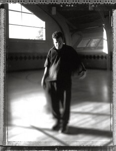 MATTHEW SWARTS A PERSON IN DARK CLOTHING STANDS ON AN INDOOR BASKETBALL COURT, HOLDING A BASKETBALL. THIS BLACK AND WHITE MATTHEW SWARTS PHOTOGRAPHY FEATURES SOFT FOCUS AND DRAMATIC LIGHT STREAMING THROUGH LARGE WINDOWS, CREATING A STRIKING VISUAL ATMOSPHERE.