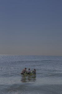 MATTHEW SWARTS A MAN, A CHILD, AND A WOMAN SIT IN A COLORFUL INFLATABLE TUBE IN THE OCEAN ON A SUNNY DAY.