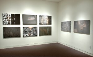 MATTHEW SWARTS EIGHT ABSTRACT AND TEXTURED ARTWORKS BY MATTHEW SWARTS ARE DISPLAYED ON TWO WHITE GALLERY WALLS, FEATURING DARK TONES, GRIDS, PATTERNS, AND FAINT HUMAN FIGURES—SUGGESTING SCENES FROM AN ANIMATION OR VIDEO.