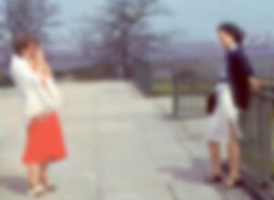 MATTHEW SWARTS A BLURRED IMAGE SHOWS TWO WOMEN STANDING ON A WALKWAY. ONE IS WEARING A WHITE CARDIGAN AND ORANGE SKIRT, THE OTHER A DARK JACKET AND WHITE SKIRT.