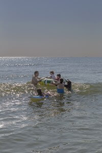 MATTHEW SWARTS A FAMILY ENJOYS A DAY AT THE BEACH, WITH CHILDREN PLAYING IN THE WATER ON A FLOAT AND BOOGIE BOARD, WHILE ADULTS ASSIST THEM.