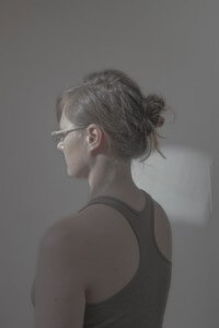 MATTHEW SWARTS A PERSON WEARING GLASSES AND A TANK TOP IS SHOWN FROM THE BACK, WITH THEIR HAIR IN A BUN.