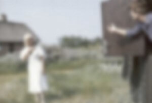 MATTHEW SWARTS A BLURRY OUTDOOR SCENE WITH A PERSON IN A WHITE DRESS STANDING ON GRASS AND ANOTHER PERSON ON THE RIGHT GESTURING, WITH A HOUSE AND GREENERY IN THE BACKGROUND.