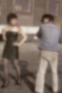 MATTHEW SWARTS A BLURRED IMAGE OF TWO PEOPLE OUTDOORS; ONE IS WEARING A BLACK DRESS AND STANDING WITH A HAND ON THEIR HIP, WHILE THE OTHER, IN A BLUE JACKET AND LIGHT PANTS, FACES AWAY. THE BACKGROUND SHOWS A BUILDING WITH WINDOWS.