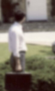 MATTHEW SWARTS A BLURRY IMAGE OF A PERSON STANDING OUTDOORS, HOLDING A BRIEFCASE, FACING A HOUSE WITH STEPS AND A WHITE DOOR. THE BACKGROUND INCLUDES SOME GREENERY AND A WALKWAY.