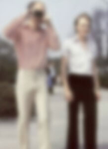 MATTHEW SWARTS TWO PEOPLE ARE STANDING OUTDOORS ON A SUNNY DAY; ONE IS HOLDING A CAMERA UP TO THEIR FACE, AND BOTH ARE WEARING LIGHT-COLORED SHIRTS AND PANTS. THE IMAGE IS BLURRED AND DETAILS ARE NOT CLEARLY VISIBLE.
