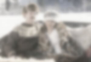 MATTHEW SWARTS A BLURRED IMAGE SHOWING TWO PEOPLE SITTING CLOSE TOGETHER, BOTH WEARING PATTERNED OR TEXTURED CLOTHING, WITH AN OUTDOOR SNOWY BACKGROUND. THEIR FACES AND DETAILS ARE NOT CLEARLY VISIBLE.