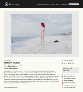 MATTHEW SWARTS A NUDE PERSON WITH A RED TOWEL WRAPPED AROUND THEIR HEAD STANDS ON A SANDY BEACH NEAR THE WATER ON A CLOUDY DAY—A SCENE REMINISCENT OF MATTHEW SWARTS, WITH DISTANT HOUSES AND GREENERY LINING THE SHORELINE.