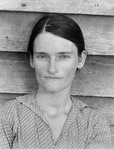 MATTHEW SWARTS A BLACK-AND-WHITE PHOTOGRAPHY PORTRAIT OF A WOMAN WITH DARK HAIR PARTED IN THE MIDDLE, WEARING A PATTERNED BLOUSE, STANDS BEFORE A WOODEN WALL, LOOKING DIRECTLY AT THE CAMERA WITH A NEUTRAL EXPRESSION—A STRIKING EXAMPLE OF VISUAL ART.
