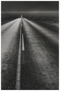 MATTHEW SWARTS A BLACK AND WHITE PHOTOGRAPH SHOWS A LONG, EMPTY HIGHWAY STRETCHING TO THE HORIZON UNDER A DARK SKY. A SINGLE CAR IS VISIBLE IN THE DISTANCE.