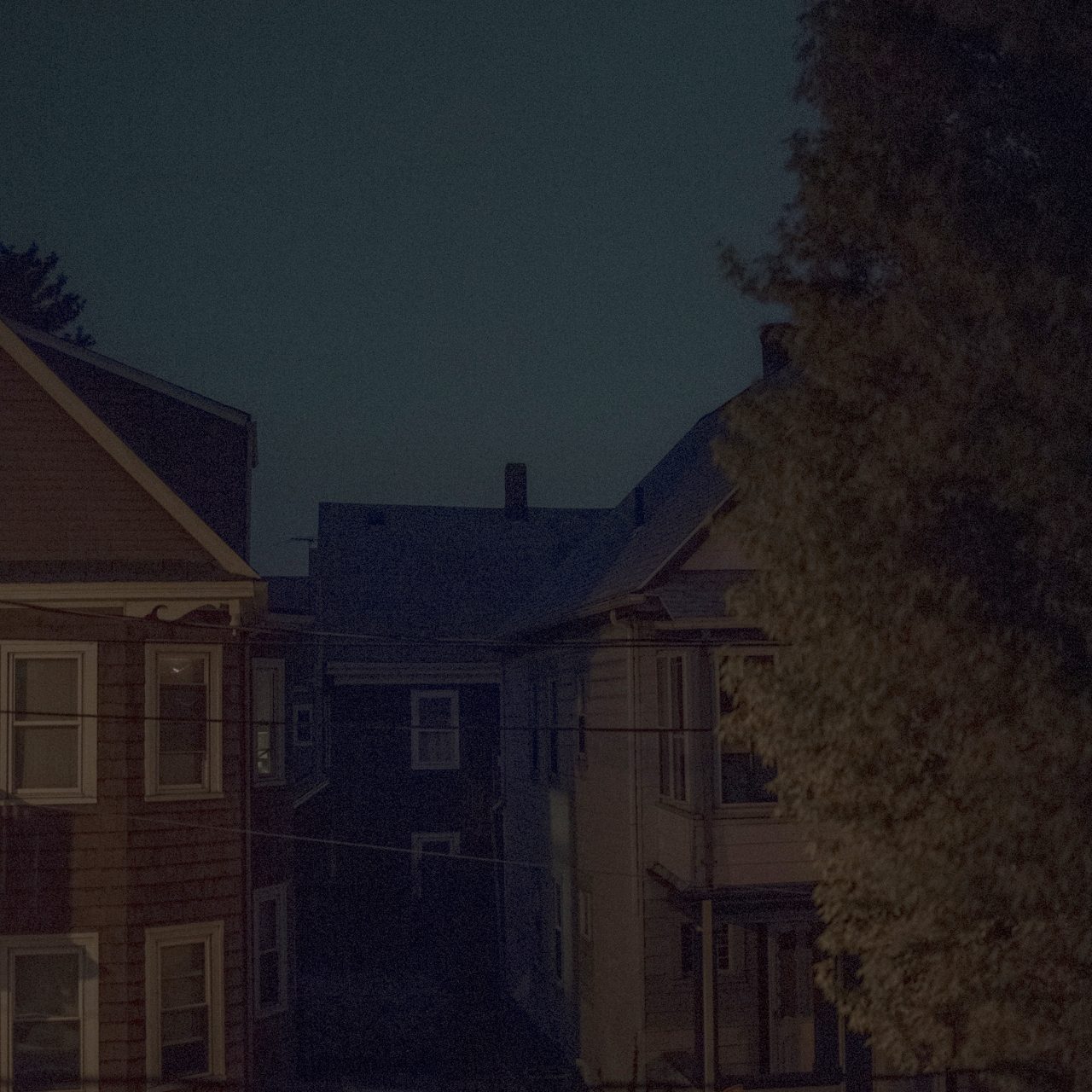 MATTHEW SWARTS A VISUAL, CONTEMPORARY SCENE AT NIGHT SHOWS TWO HOUSES WITH DARK WINDOWS, A NARROW DRIVEWAY BETWEEN THEM, A PARKED CAR, AND A LARGE TREE ON THE RIGHT, ALL UNDER A DARK BLUE SKY.