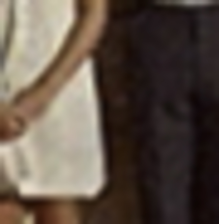 MATTHEW SWARTS A blurred photo in a contemporary photography style shows part of two people standing side by side—one in a light-colored dress, the other in dark pants—with their faces and upper bodies out of frame, evoking modern art sensibilities.