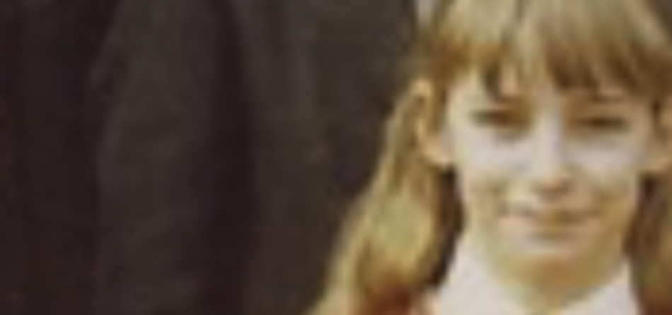 MATTHEW SWARTS A blurry, close-up photography shot of a young person with long light brown hair and bangs, wearing a white shirt and a red tie, standing outdoors.