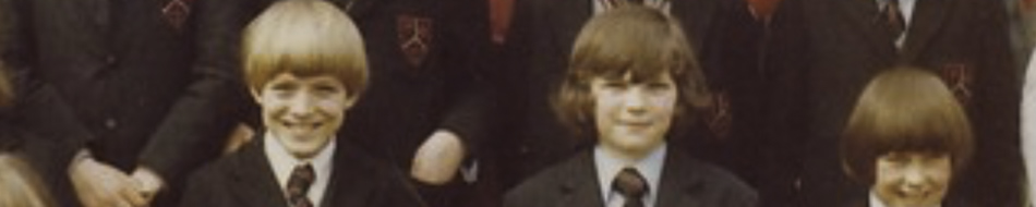 MATTHEW SWARTS A group of school children in uniform, wearing blazers and ties, posing and smiling for a class photo. The image, reminiscent of ART by photographer Matthew Swarts, focuses on three boys in the front row with bowl-cut hairstyles.
