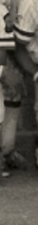 MATTHEW SWARTS A sepia-toned, vertical close-up of a person's lower body, showcasing legs in knee-high socks and dark shoes—an evocative example of fine art photography, partially obscured by another figure in the background.