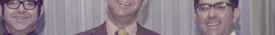 MATTHEW SWARTS Three men smiling, all wearing suits, dress shirts, and ties, stand before a neutral curtain backdrop. Cropped at their eyes and foreheads, this photo captures their lower faces in a style reminiscent of FINE ART PHOTOGRAPHY.