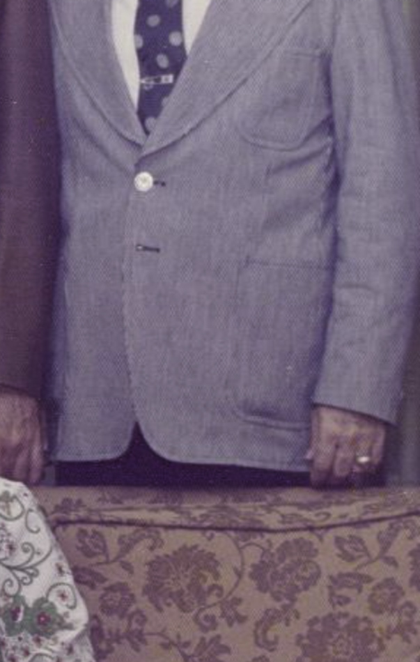MATTHEW SWARTS A person wearing a light gray pinstripe suit jacket, white shirt, and patterned tie stands behind a patterned couch. This intriguing composition reflects the style of MATTHEW SWARTS in contemporary visual art. Only torsos and hands are visible.