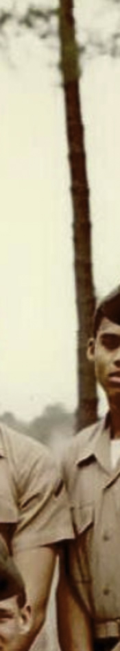 MATTHEW SWARTS A cropped, vintage photo evokes the feel of visual art, showing two people in tan military uniforms standing outdoors near a tree. Only their torsos and partial faces are visible, adding an air of mystery to this ARTIST-inspired scene.