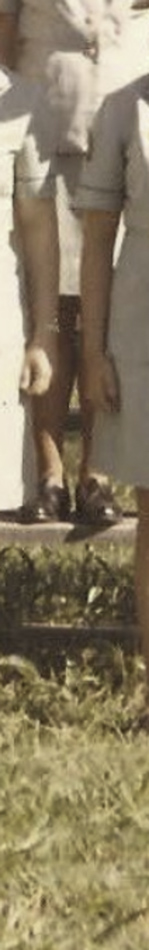 MATTHEW SWARTS A cropped vintage photo by ARTIST MATTHEW SWARTS focuses on a person's lower legs and feet in brown sandals and light-colored shorts, standing on grass beside another person.