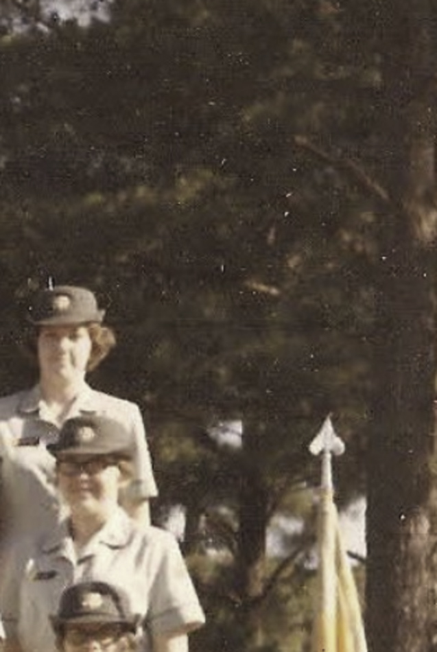 MATTHEW SWARTS Three people in light-colored uniforms and hats stand outdoors in front of tall pine trees. The upper bodies of two are visible, with part of a flag on the right—a composition reminiscent of artist Matthew Swarts' approach to art and observation.