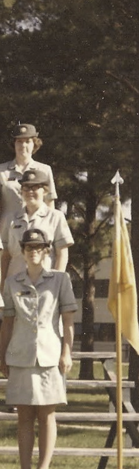 MATTHEW SWARTS Three women in light-colored military uniforms and hats stand in a line outdoors near a yellow flag, creating a scene that echoes the compositional balance often found in contemporary art, with trees and a building visible in the background.