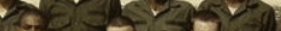 MATTHEW SWARTS A cropped, partially blurred image by artist Matthew Swarts shows six people in green military uniforms, standing and sitting close together. Only their upper bodies and faces are visible.