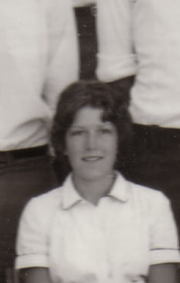 MATTHEW SWARTS A black and white photo in the style of fine art photography shows a young person with short, wavy hair and a light-colored collared shirt, seated before others whose torsos are partially visible in the background.