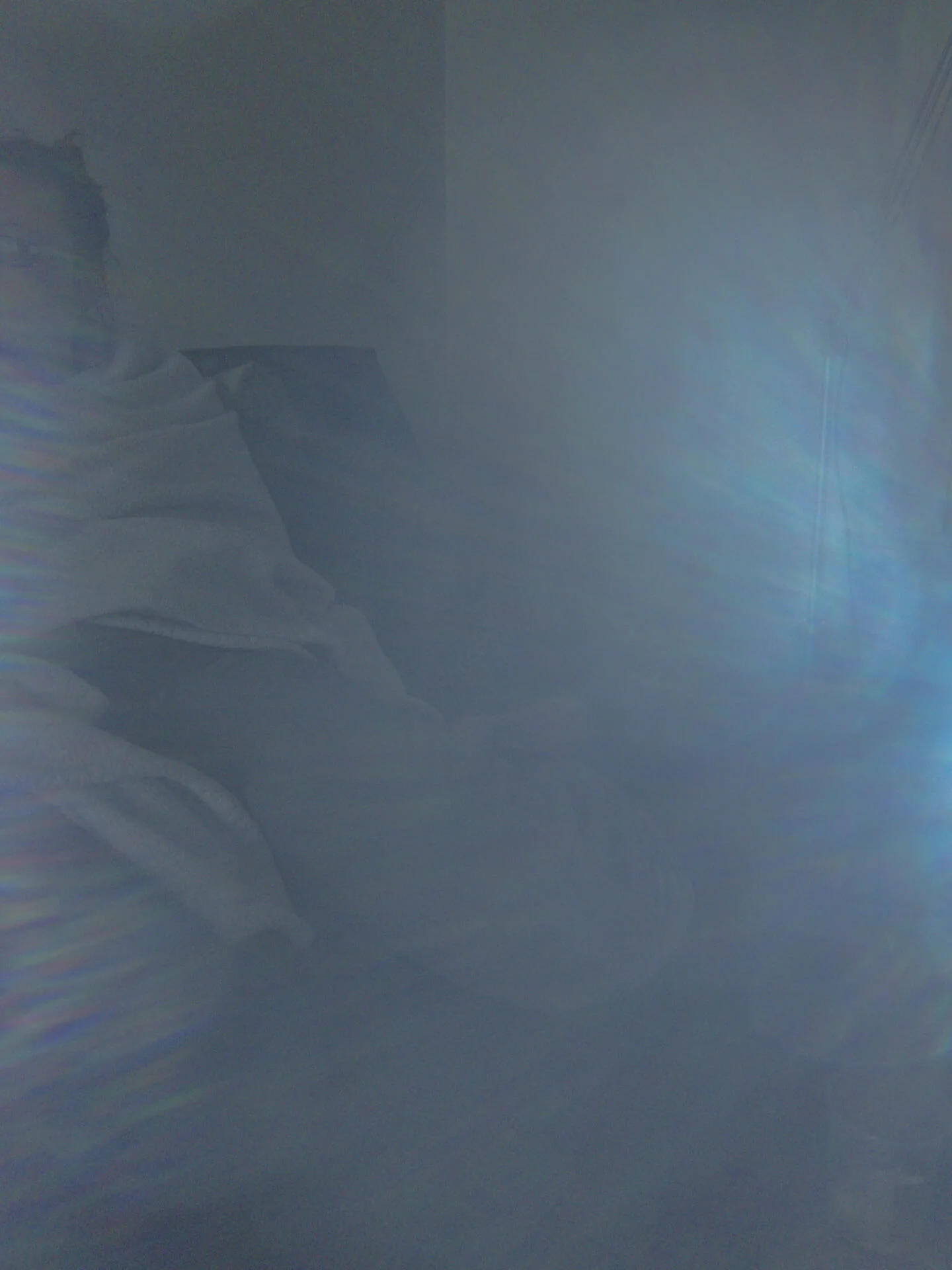 MATTHEW SWARTS A person sits on a chair covered in a blanket, partially obscured by a blue and white light glare that fills most of the image, creating a hazy, dreamy effect reminiscent of contemporary art by Matthew Swarts.