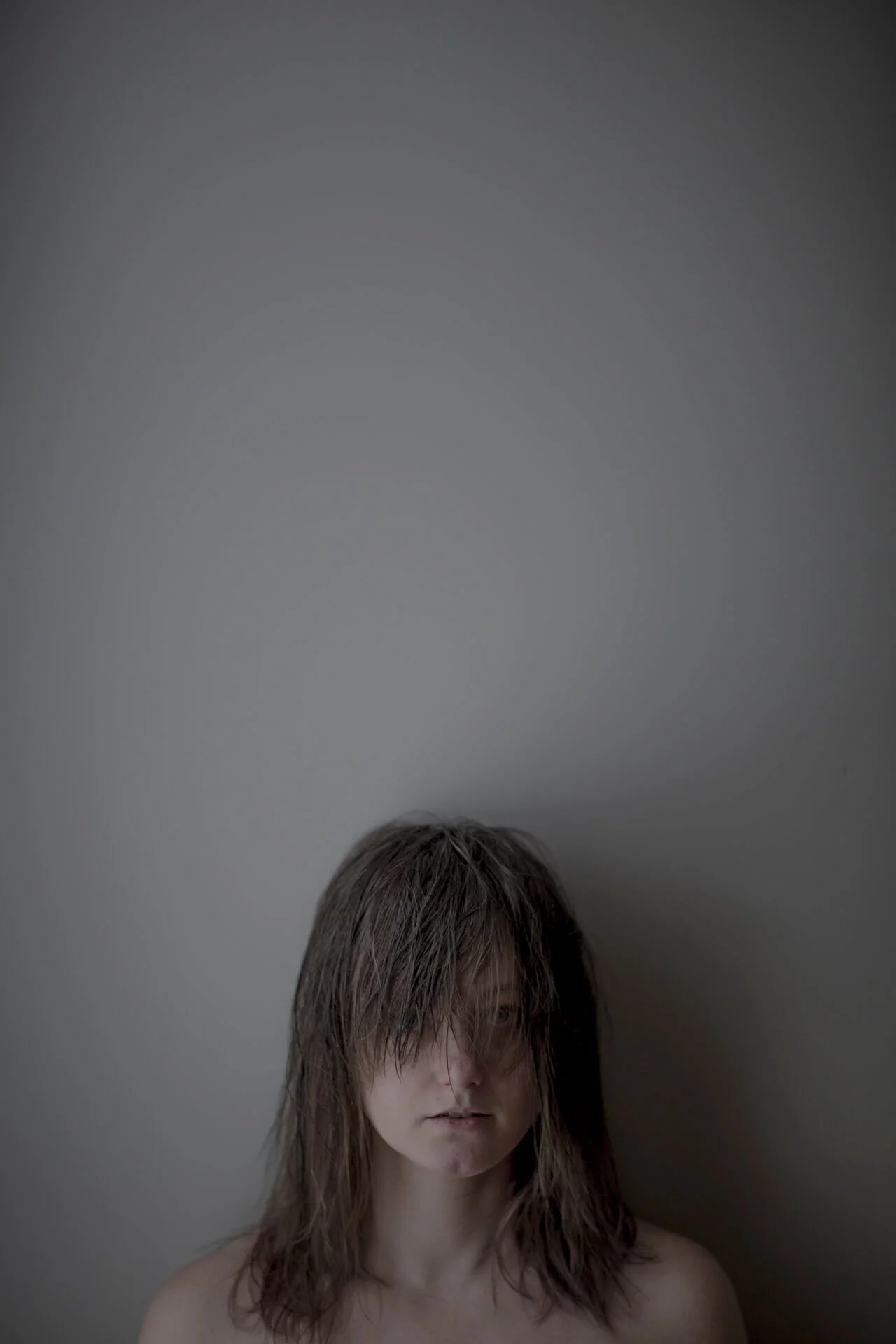 MATTHEW SWARTS A person with long, messy hair covering their eyes stands against a plain gray wall, looking downward with a somber expression—a striking VISUAL evoking contemporary artist sensibilities. The upper part of the image is mostly empty space.