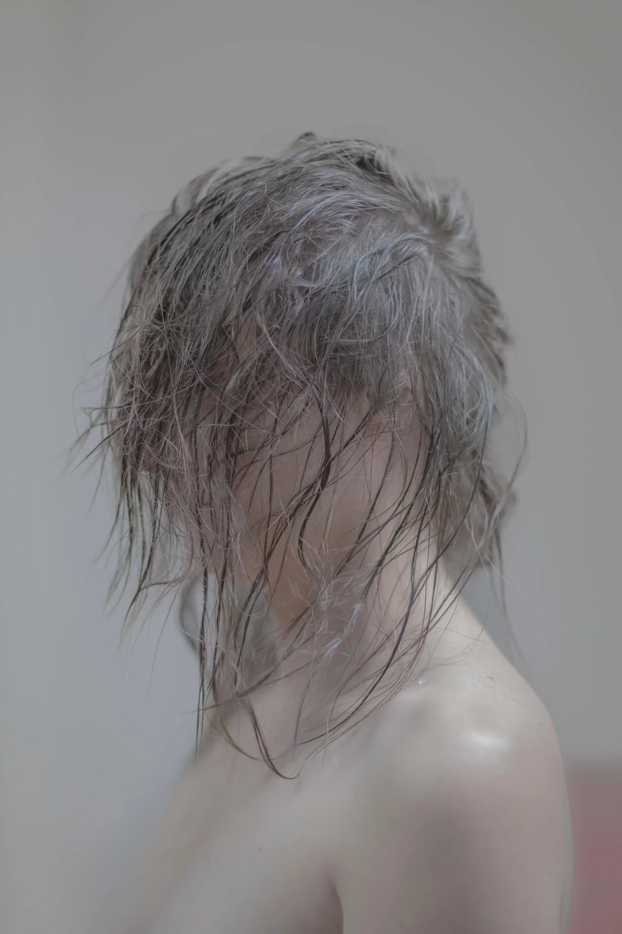MATTHEW SWARTS A person with wet, tousled hair covers most of their face, standing against a plain, softly lit background. Their shoulders are bare, evoking the enigmatic style of artist Matthew Swarts and his introspective art.