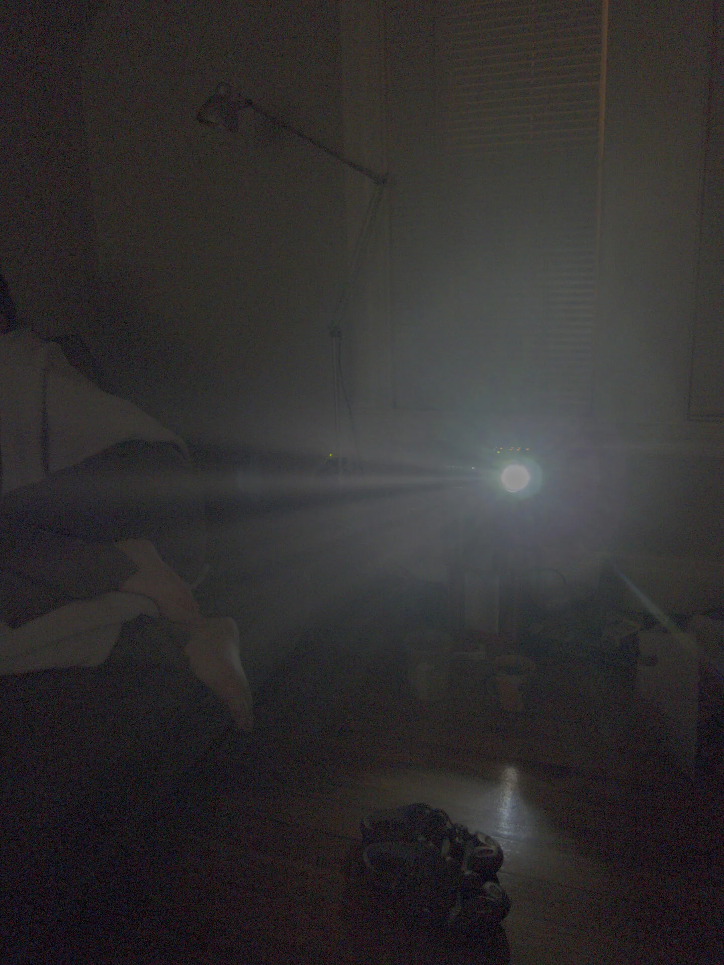 MATTHEW SWARTS A dimly lit room with a bright light or projector shining toward the camera, casting visual beams. A person’s legs rest on a couch to the left, and scattered objects are on the wooden floor—captured by photographer Matthew Swarts.